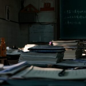 Dimly lit office space filled with messy stacks of papers and books on desks, suggesting a busy academic or work setting.