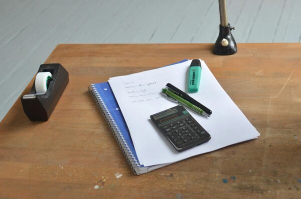 A neat workspace featuring a calculator, notebook, and stationery essentials on a wooden desk.