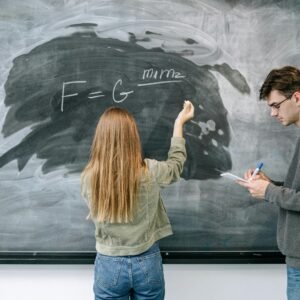 Two students discuss and solve a physics equation on the chalkboard.