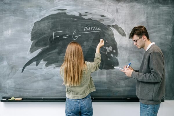 Two students discuss and solve a physics equation on the chalkboard.